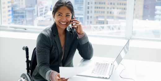 Frau im Rollstuhl telefoniert an einem barrierefreien Arbeitsplatz