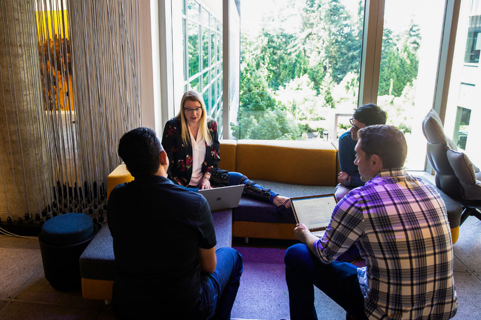 Vier Personen sitzen in einer Sitzecke. Sie halten Laptops in den Händen und sprechen miteinander.