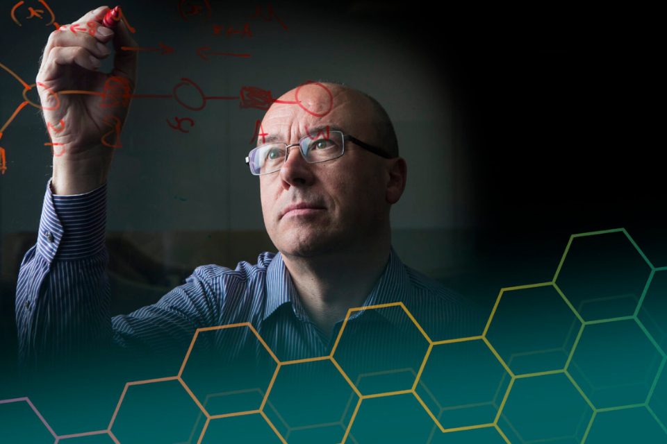 Christopher Bishop zeichnet an eine transparente Wand umgeben von Molekülen.