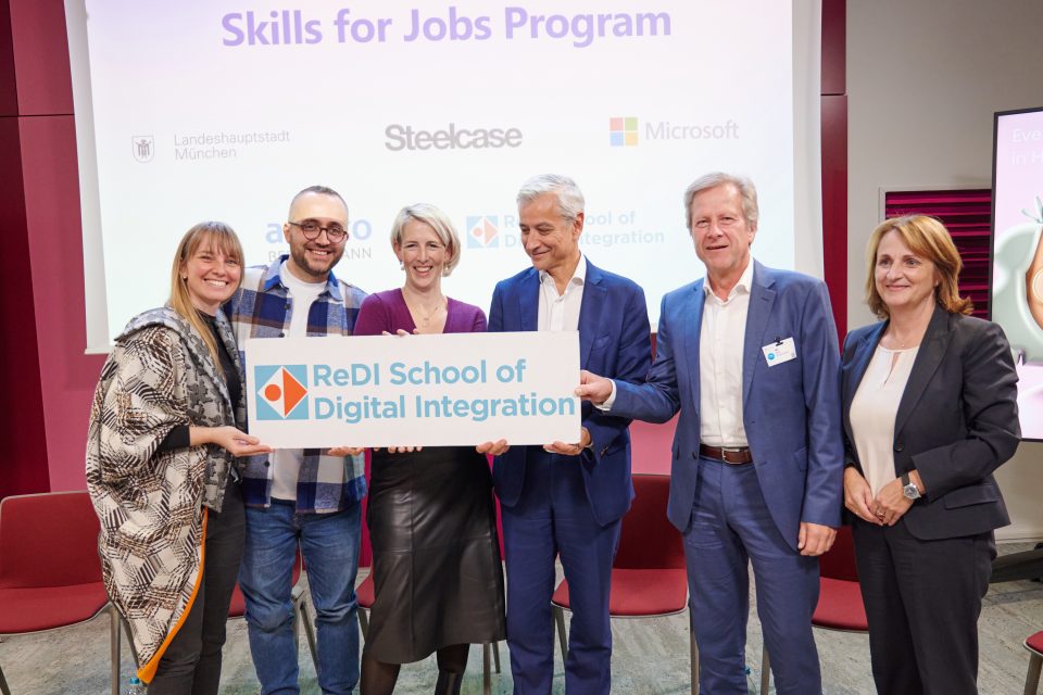 Sechs Personen stehen in einer Reihe und halten ein Schild mit dem Logo der REDI School of Digital Integration in den Händen.