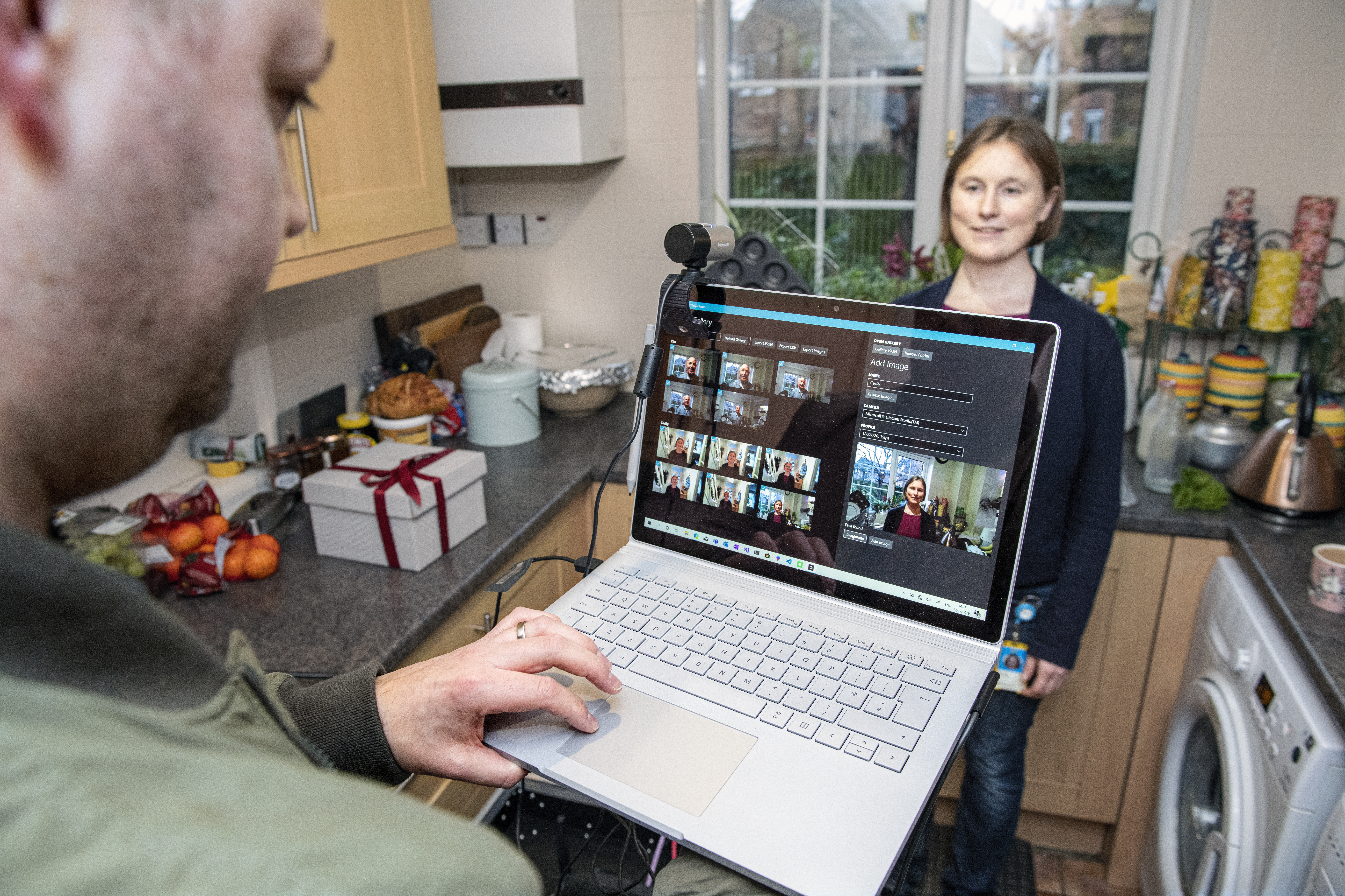 Cecily Morrison de pie en una cocina es registrada en el sistema Project Tokyo con Martin Grayson detrás de una computadora Microsoft Surface Book con una webcam integrada