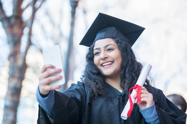 Joven estudiante recién graduada con un teléfono en la mano