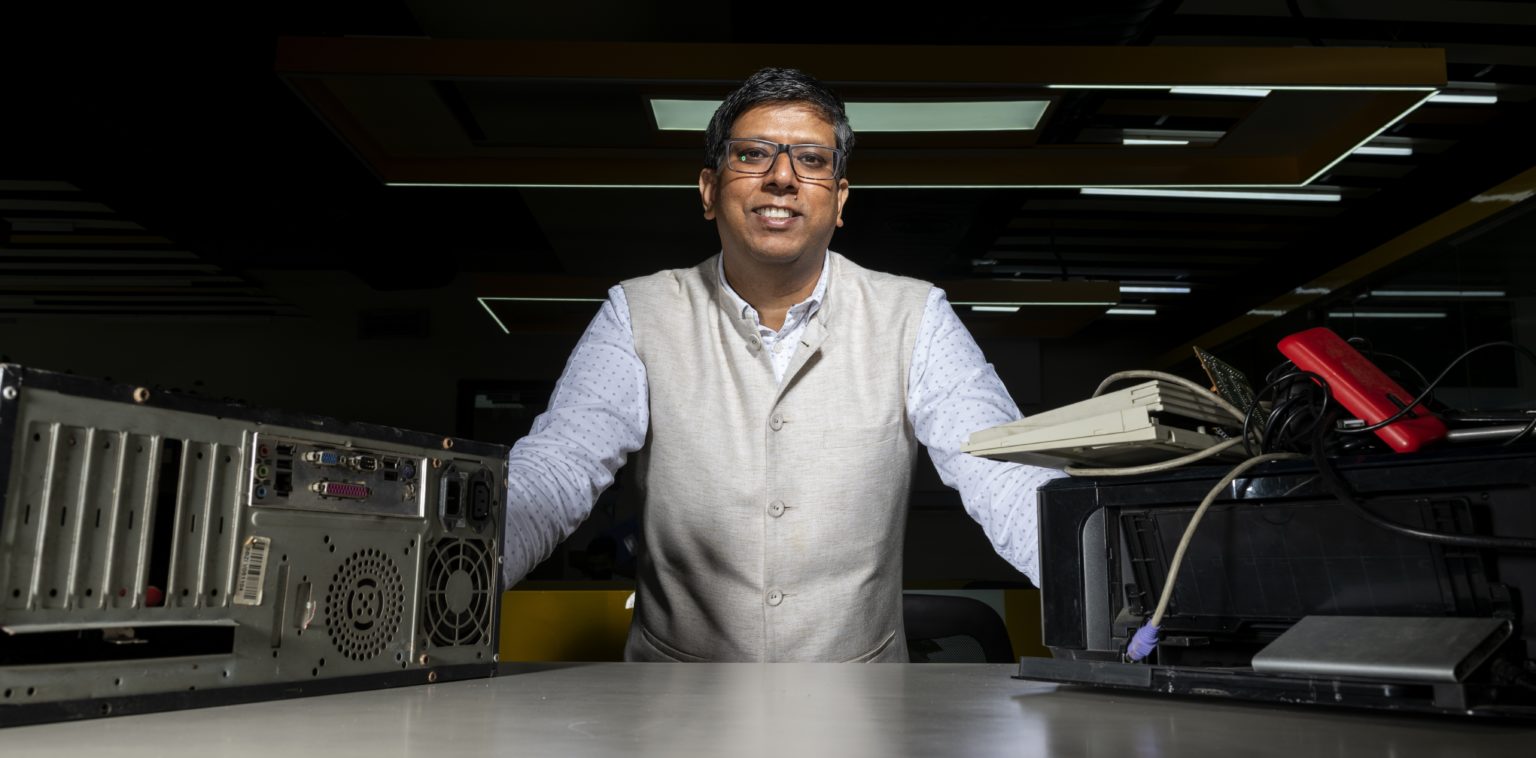 un hombre mira a la cámara con componentes descartados de PC en el fondo