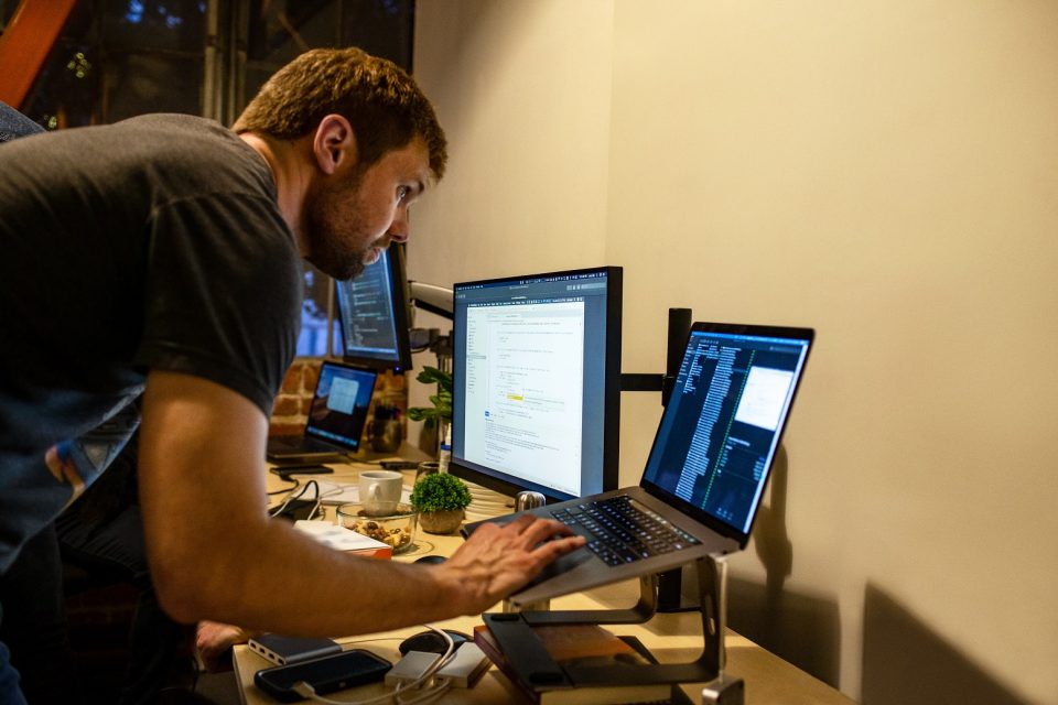 Un hombre frente a unos monitores y una laptop