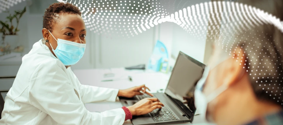 Una doctora teclea en una laptop y observa a un paciente