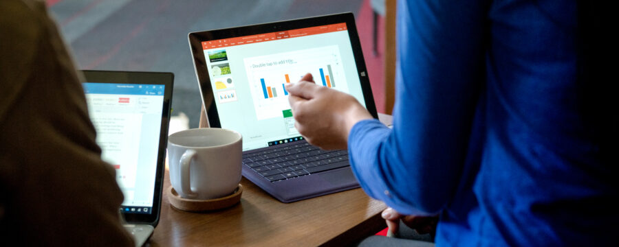 Dos computadoras portátiles abiertas sentadas en la mesa frente a dos figuras, con una taza de café entre ellas.