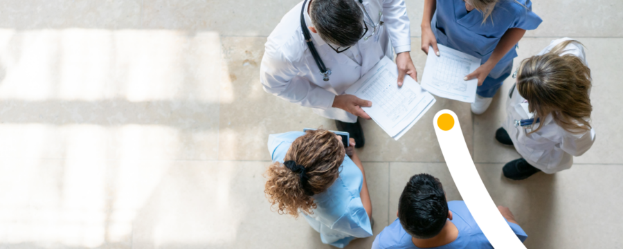 Cinco profesionales médicos parados en círculo revisan un gráfico.