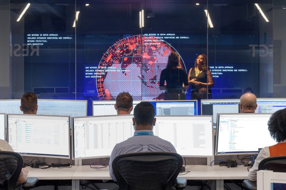 Expertos en ciberseguridad en una sala con computadoras y pantallas gigantes