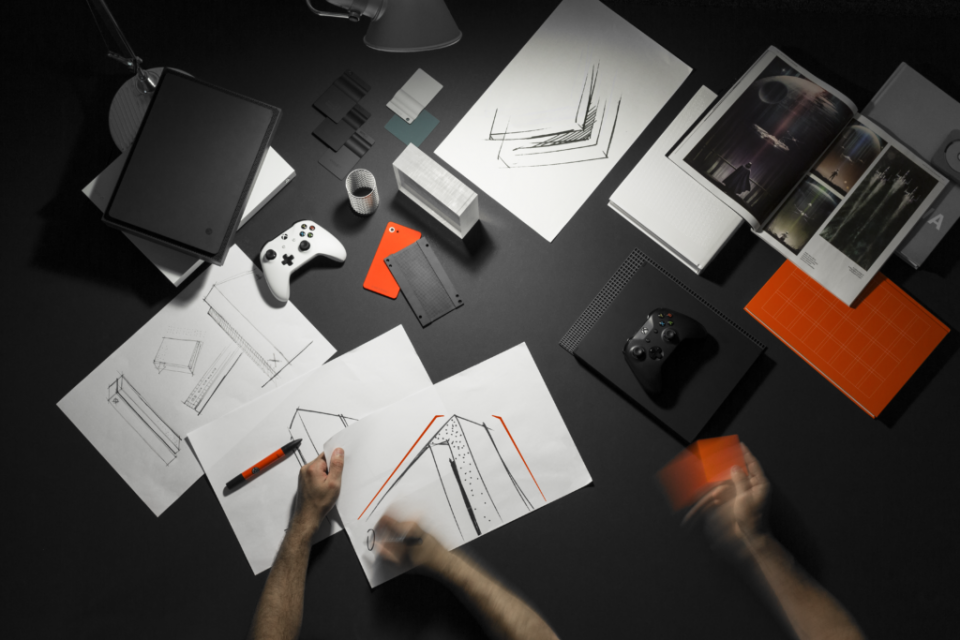 Toma cenital de una persona dibujando bocetos de Xbox junto a un control blanco
