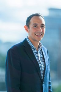 Retrato de un hombre sonriendo, con blazer azul y camisa a cuadros