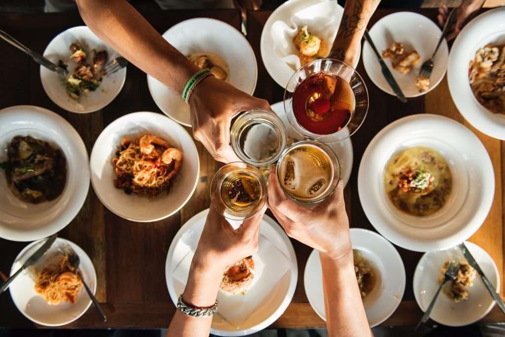 Mesa posta para o jantar e mãos elevam copos num brinde.
