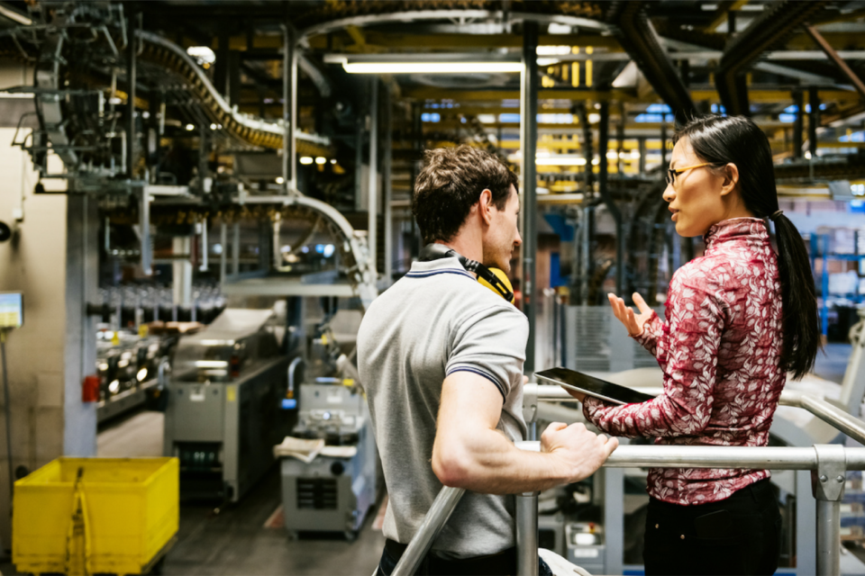 Homem e mulher conversam em um ambiente de chão de fábrica.