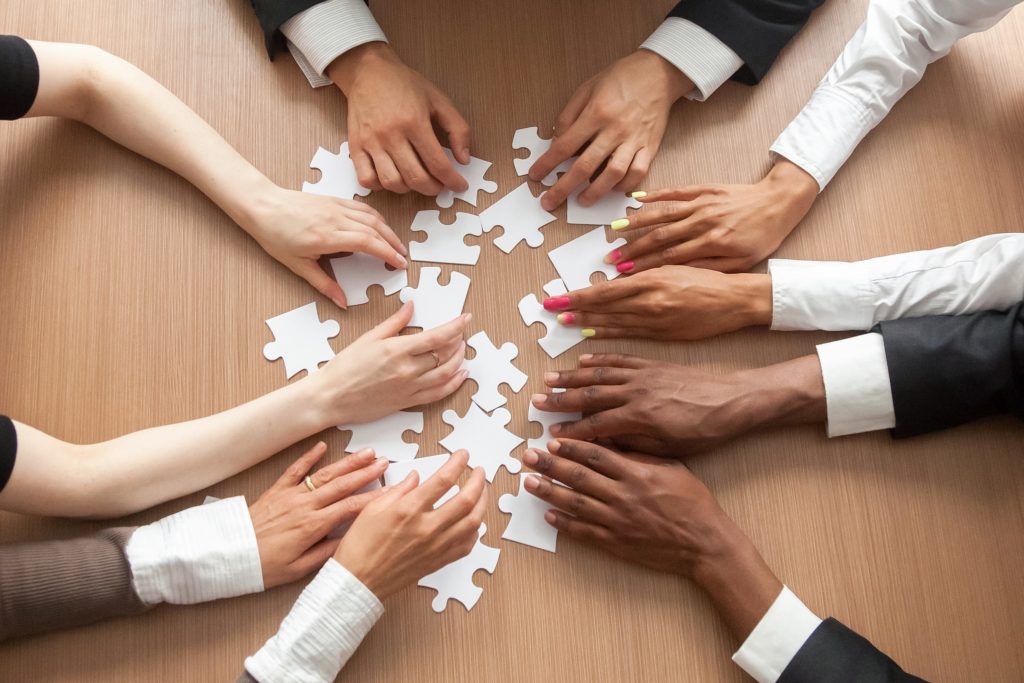 Mãos de pessoas montando um quebra-cabeças sobre uma mesa.