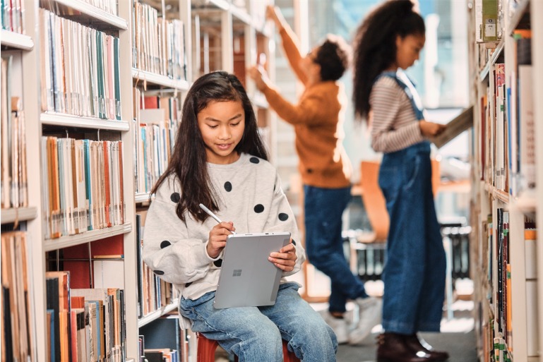 Garotas com livros e computador na biblioteca.