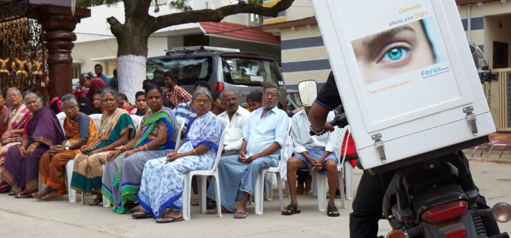 Pessoas na Índia observam a chegada da moto com o equipamento da Forus Health.