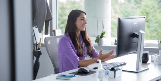 A female employee talking on a video call with hand sanitizer on her desk, socially distancing from others