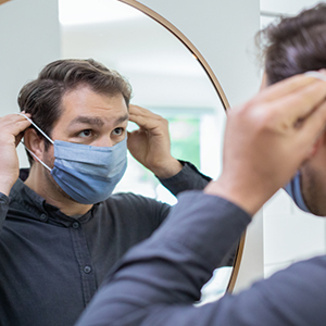 homem olhando no espelho e colocando a máscara