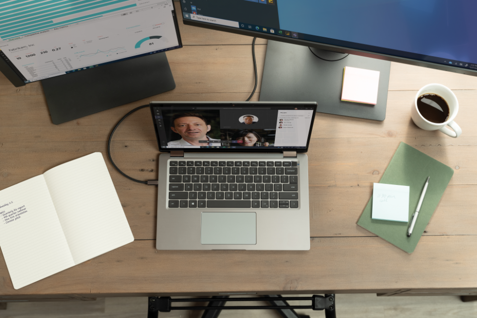 mesa de home office com dois computadores e um notebook com videoconferência aberta