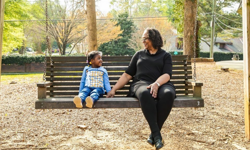 mulher sentada no banco sorrindo e segurando a mão de criança sentada