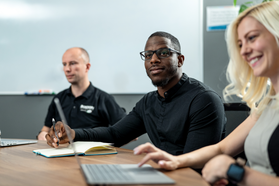 um homem branco, um negro e uma mulher loira sentados em uma mesa