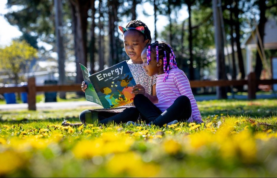 duas meninas sentadas em jardim e lendo livro