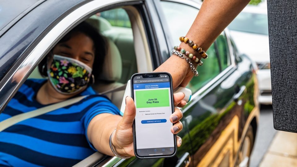 mulher de máscara e dentro do carro mostrando app no cel