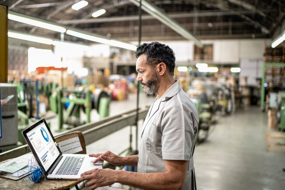 Homem trabalha em frente a um notebook em uma indústria