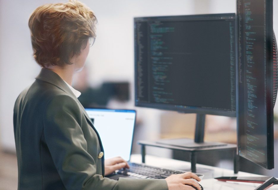 Mulher trabalha com notebook e computador em sua frente