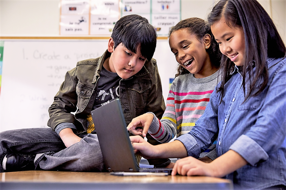 On eboys and two girsl students smile as tehy look at a laptop together.