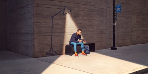 A man sits undera spotlight looking at a device in his hand.