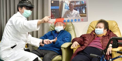 A doctors holds male patinets hand while wearing a HoloLens headset