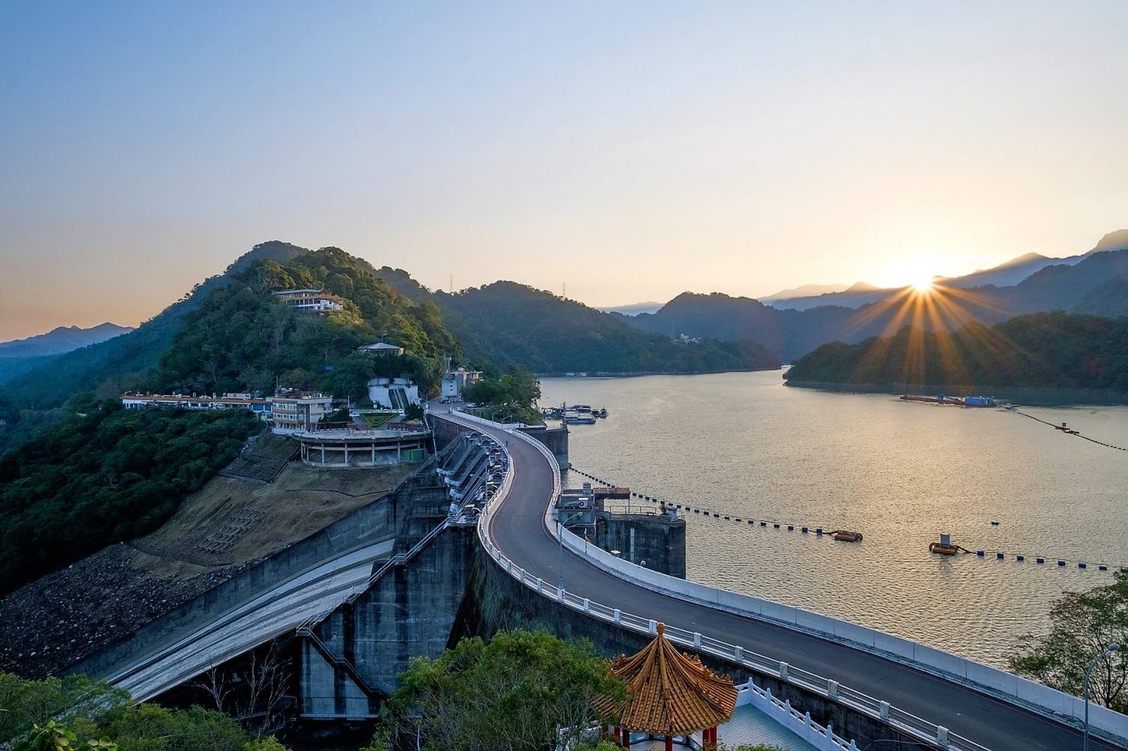 Sun rising over a dam and lake.