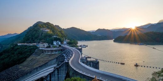 Sun rising over a dam and lake.