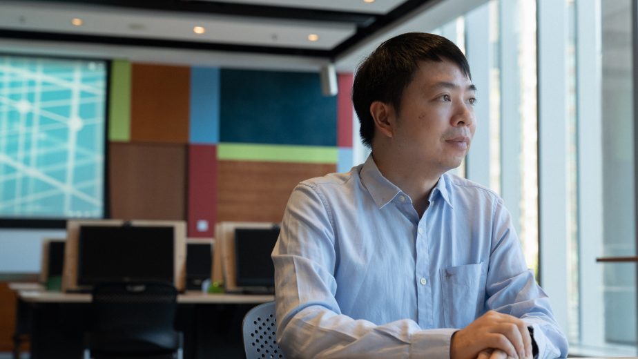 Photo of a man sitting at a table in an office, looking out the window