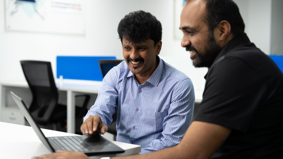 Photo of two men sitting at a desk looking at a computer