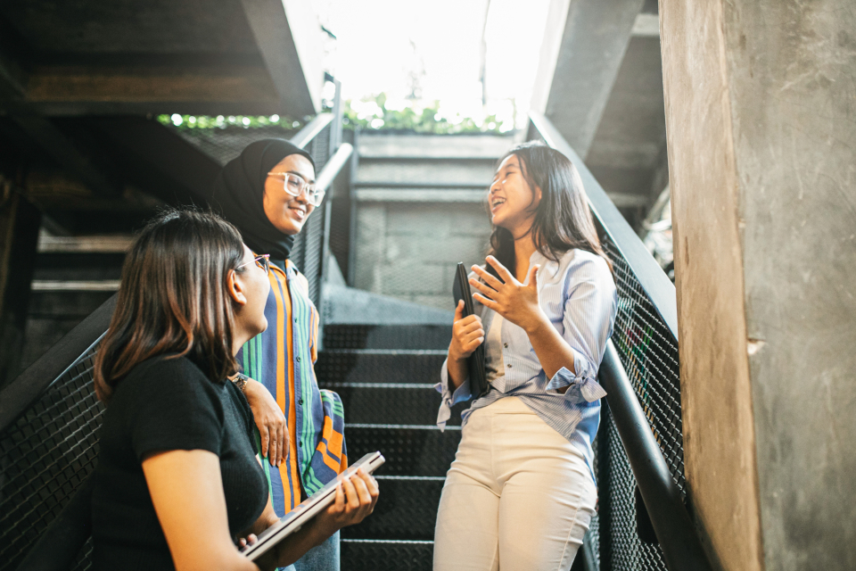 Three women discussing ideas while standing on the stairs, reflecting a dynamic workplace environment.