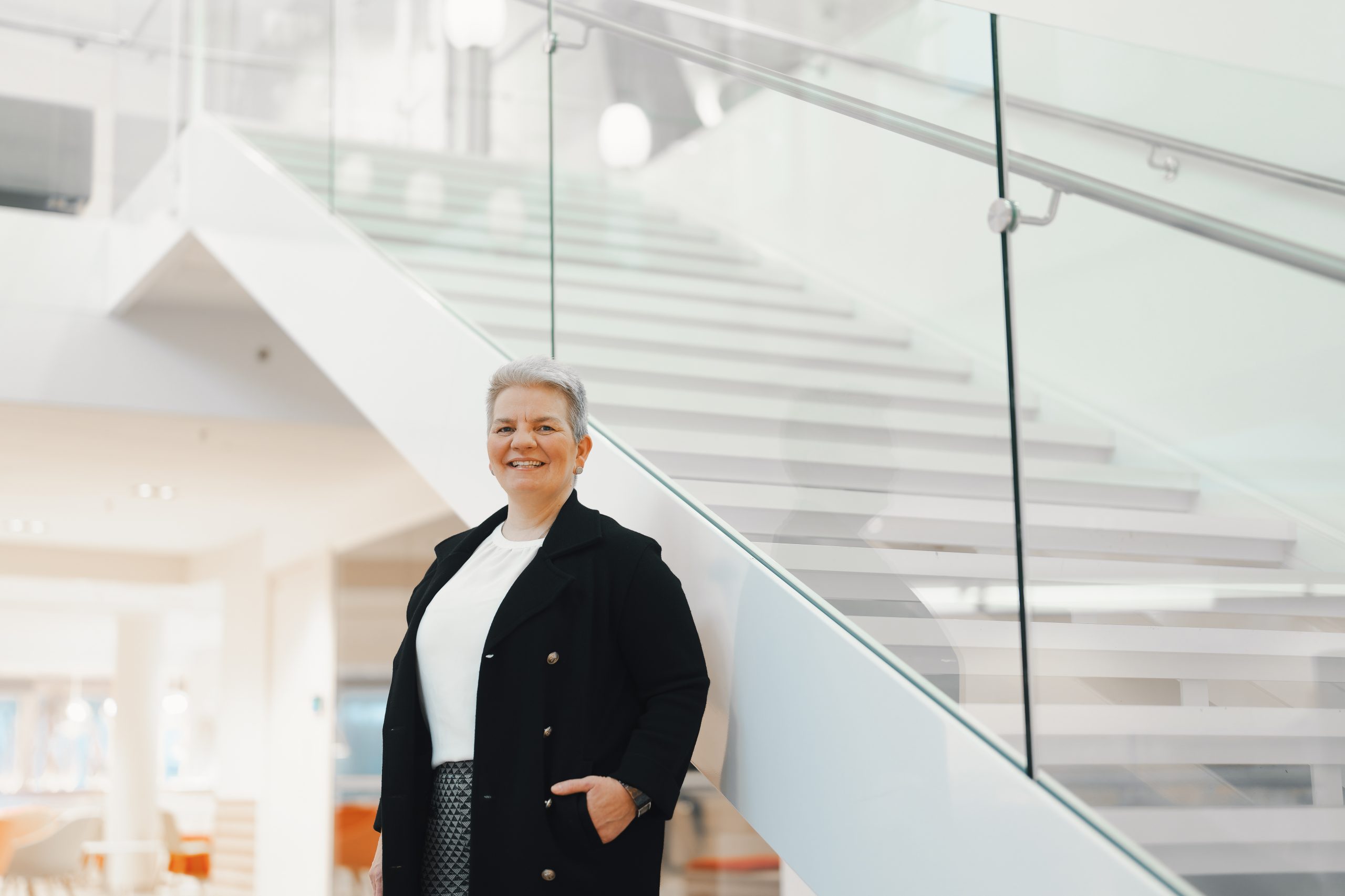 Hanna Kivelä seisoo kädet taskussa ja katsoo hymyillen kameraan. Taustalla valkoiset portaat ylöspäin.