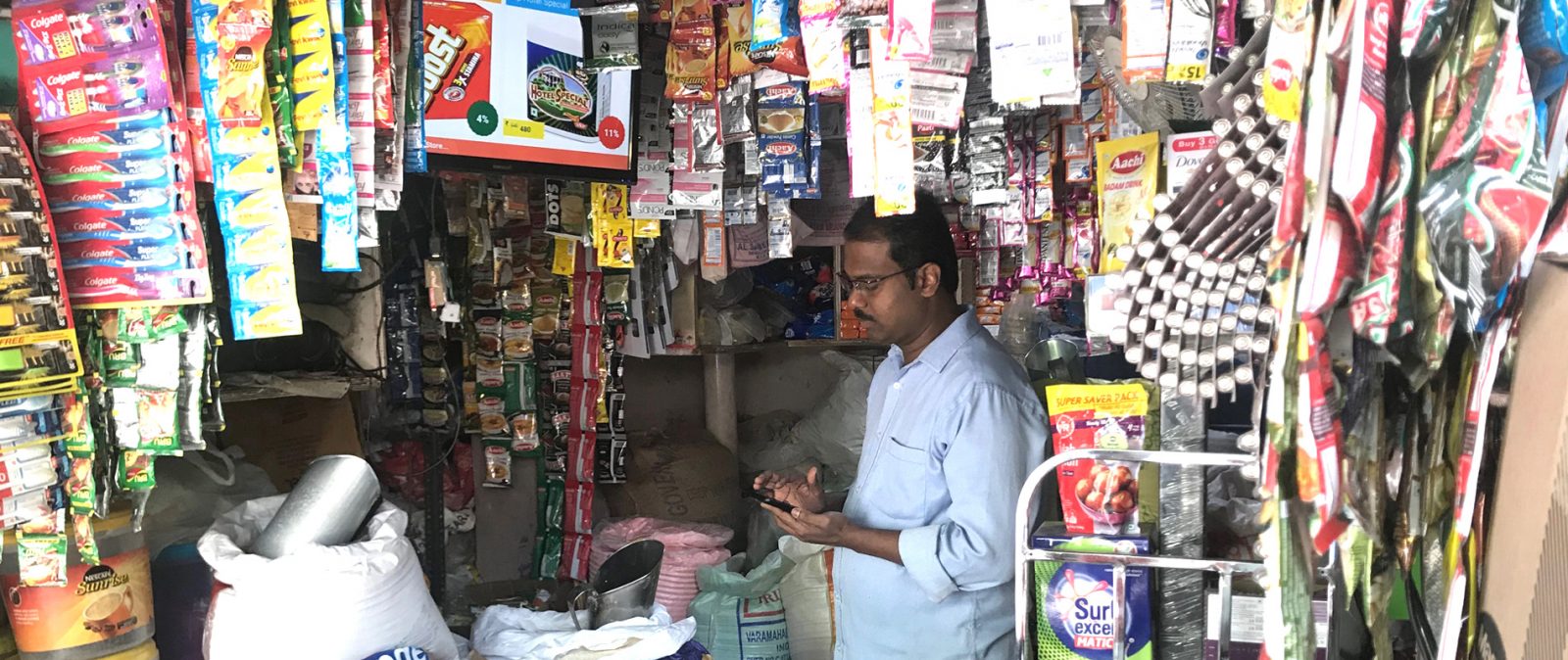 Kirana store owner manages the advertisements on the LED screen in his small store.