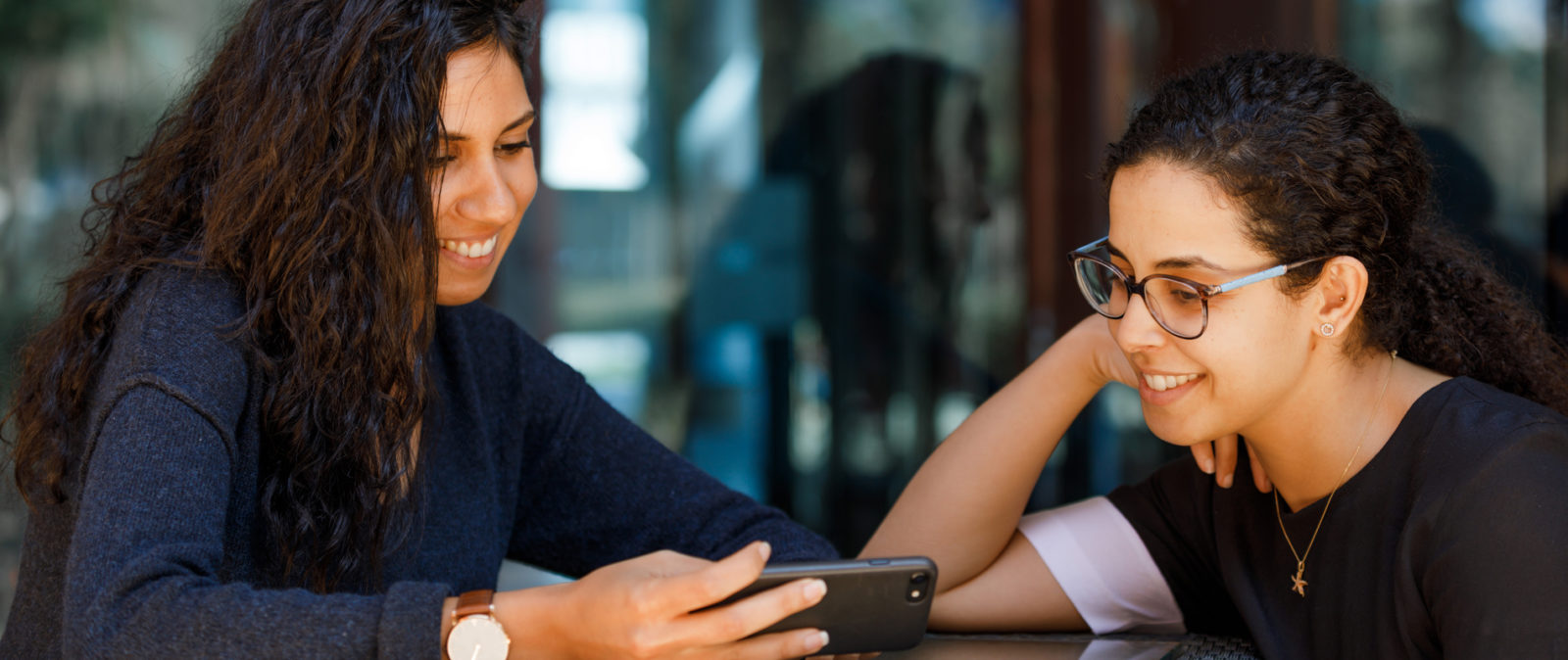 Two women smiling while looking at the mobile screen