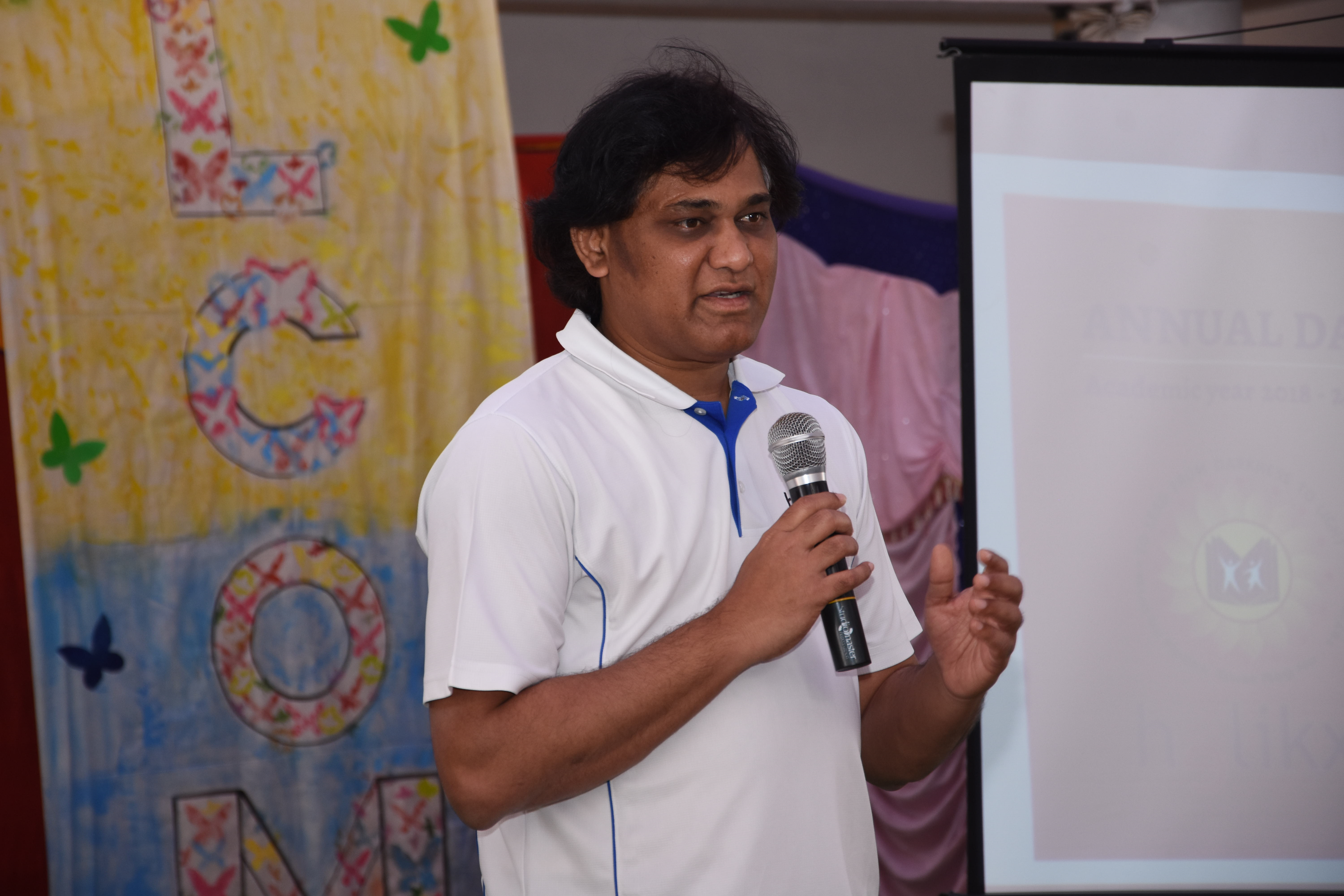 A photo of Senthilkumar holding a mic and talking to an audience