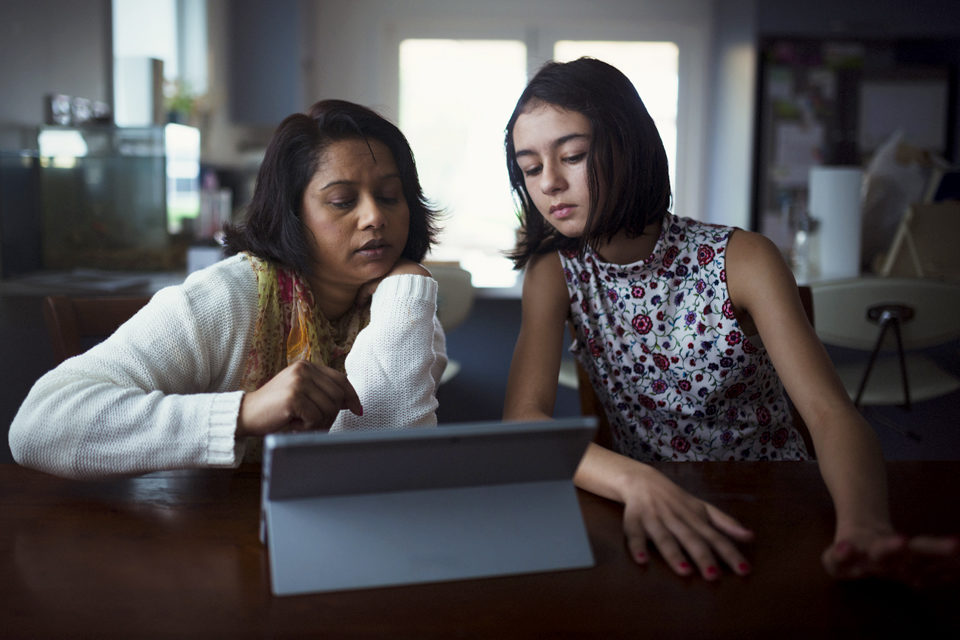 A mother and daughter duo using a tablet computer at home.