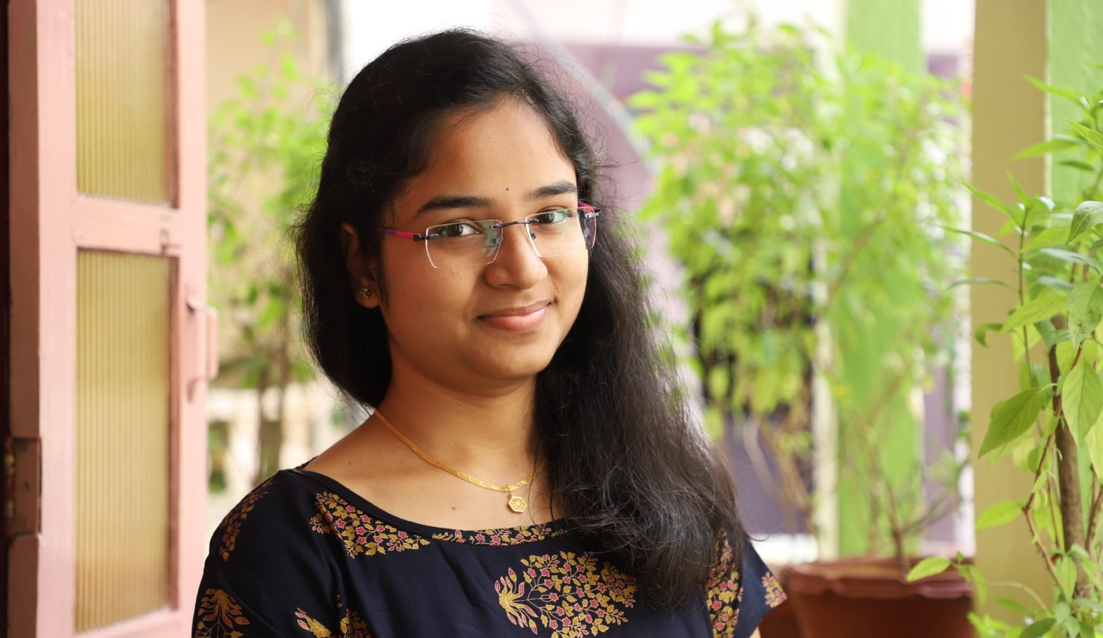Photo of a girl smiling at the camera with potted plants in the background