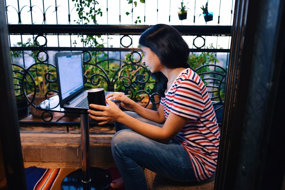 Photo of a woman sitting in her balcony working on a laptop