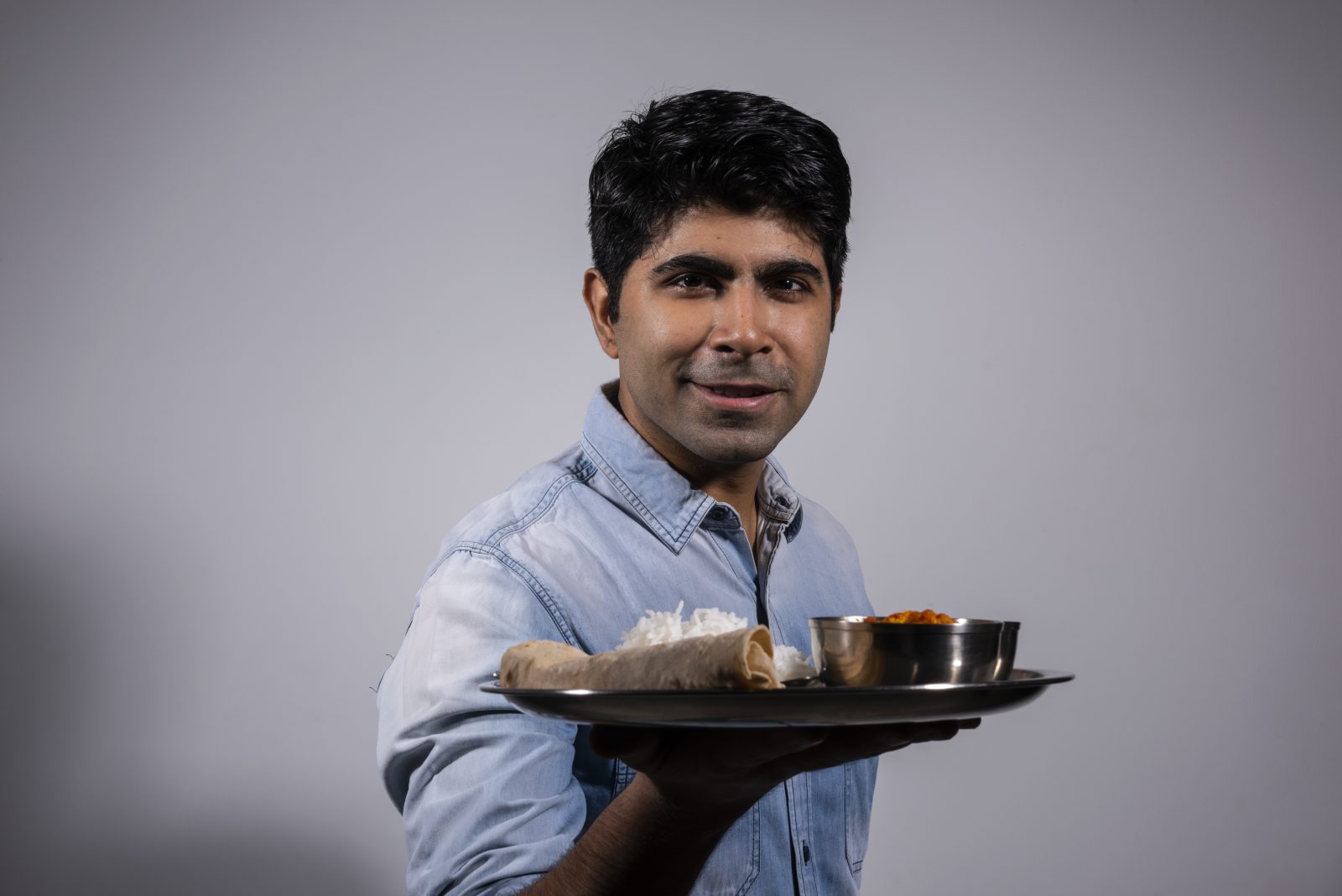 a man wearing a blue denim shirt holding a plate of food