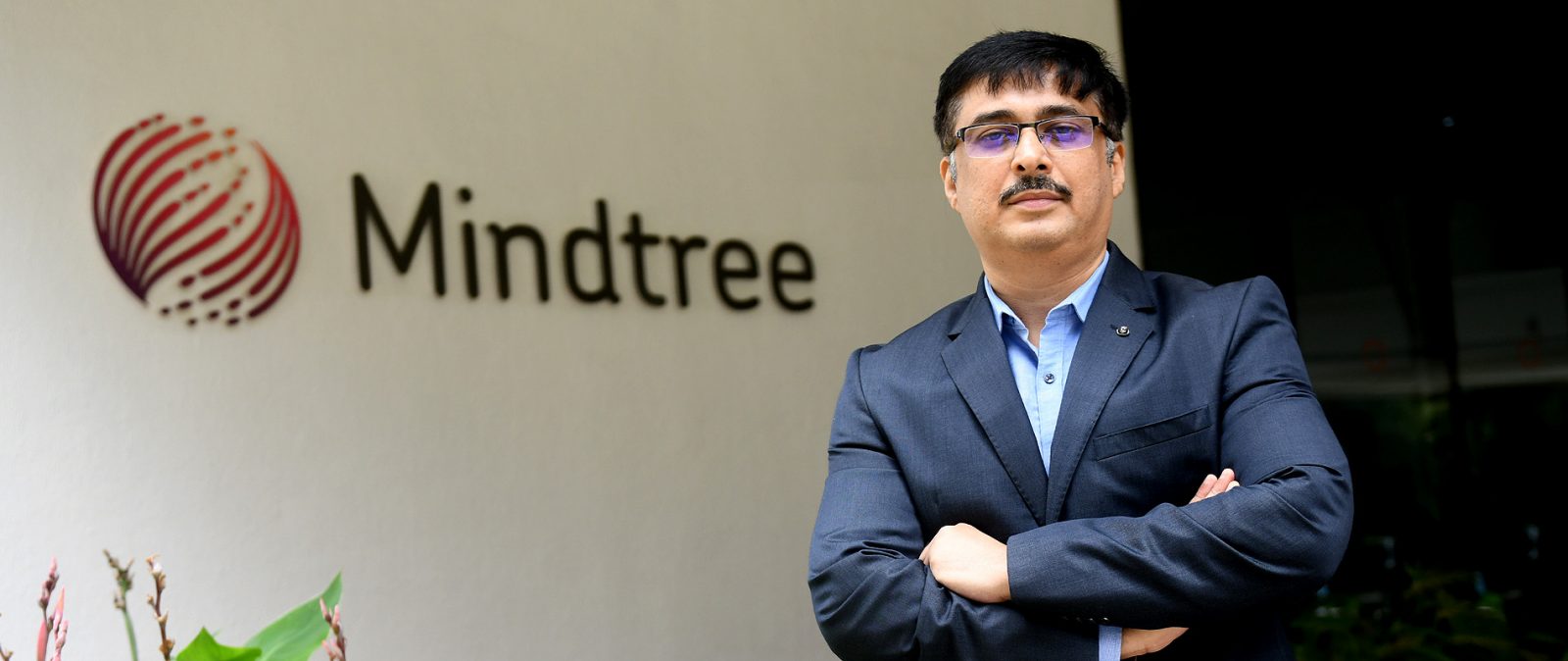 a man wearing a blue jacket with the mindtree logo in the background