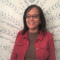 a woman wearing spectacles and a red jacket smiling at the camera