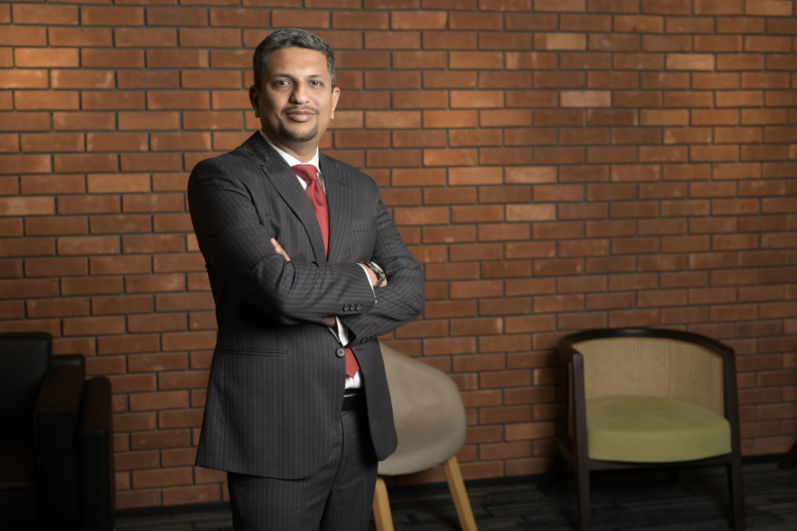 a man wearing a black suit and red tie smiling while looking at the camera