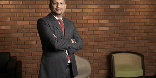 a man wearing a black suit and red tie smiling while looking at the camera