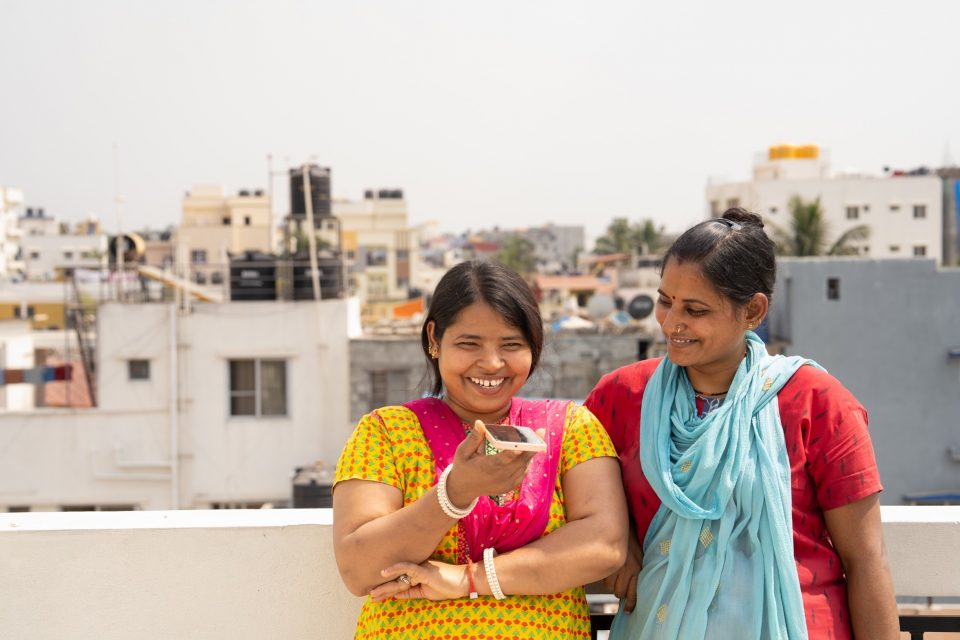 Two women resting against a parapet speaking into a phone