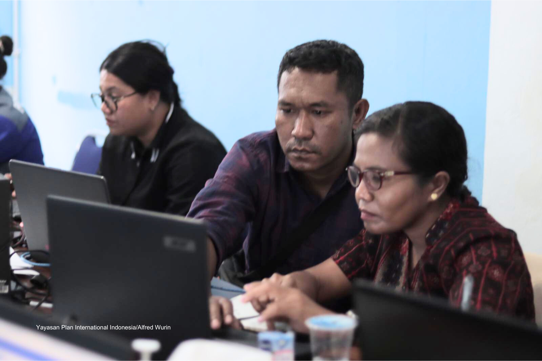A male guiding a woman with glasses to work with her laptop